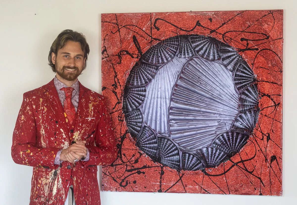 Dieses Bild von Oliver Hojas ist inspiriert vom britischen Künstler Damien Hirst. Man sieht einen Mann, der neben einem abstrakten Bild steht.